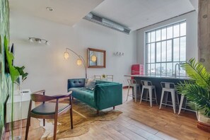 Un salon moderne avec un canapé de couleur turquoise, des chaises en bois, un coin repas doté de tabourets de bar et une grande fenêtre offrant une vue sur la ville.