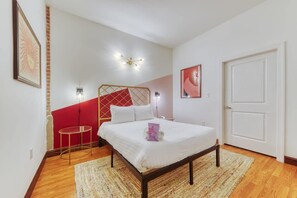 Un dormitorio con cama, una mesita redonda, una pared de acento roja y una puerta.
