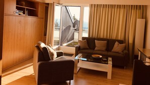 A modern living room with a sofa, armchair, and coffee table. There is a wooden cabinet and a large window with curtains. - Ferienwohnung Frohwein (Winterberg)