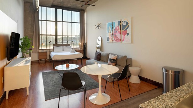 Una habitación de hotel moderna con cama, sofá, mesa de comedor, sillas, televisor y obras de arte en la pared.