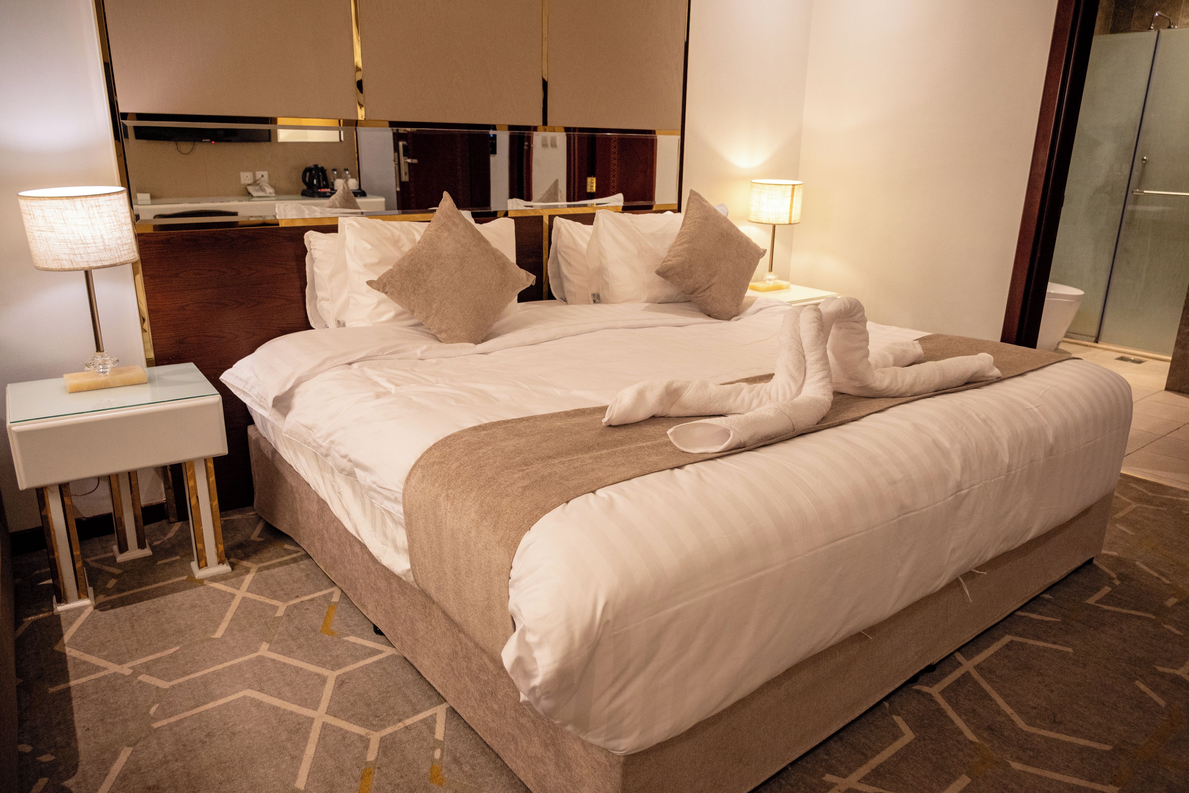 A hotel room with a large bed, two bedside tables, a desk, and a mirror.
