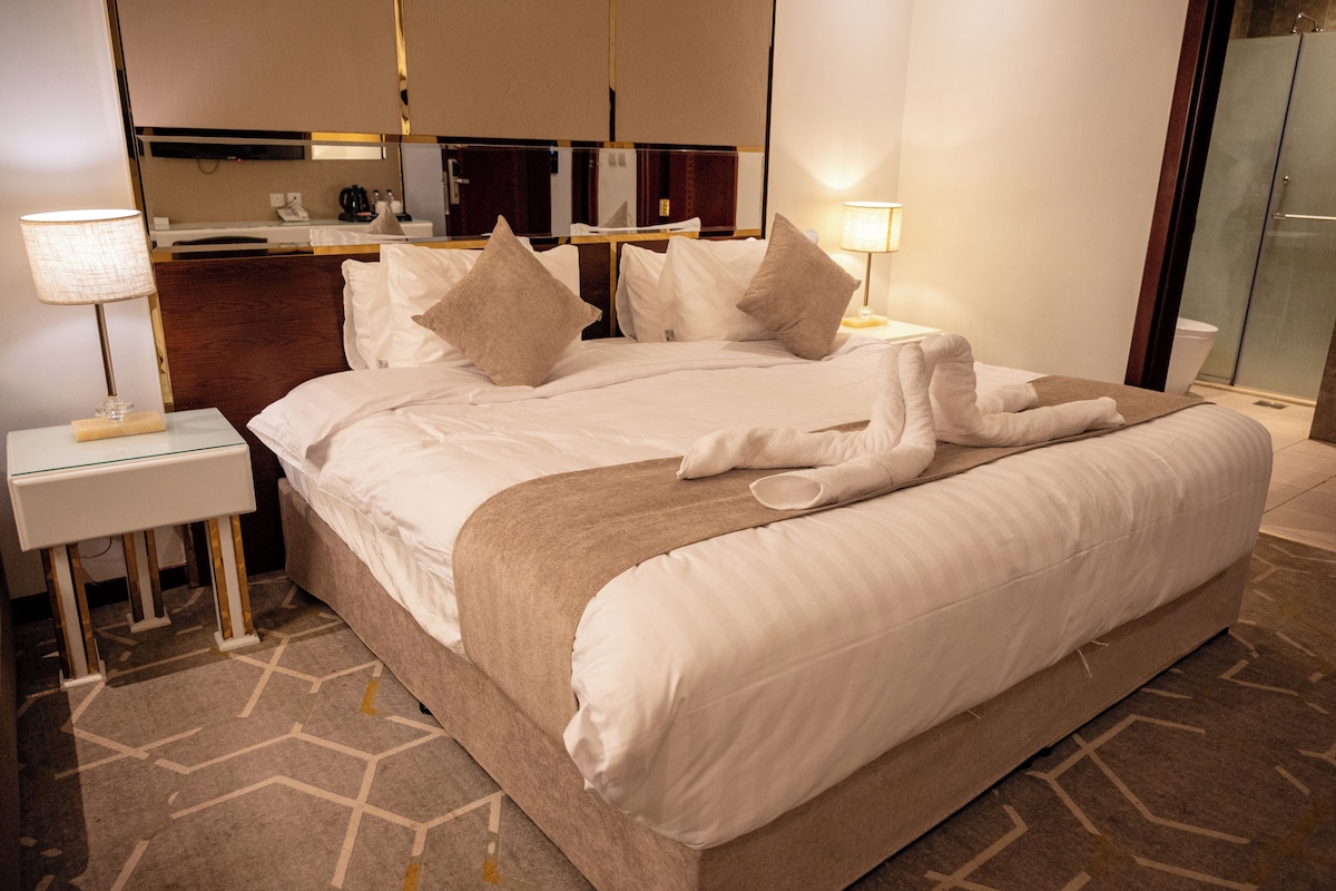 A hotel room with a large bed, two bedside tables, a desk, and a mirror.