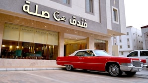Ein Gebäude mit einer arabischen Beschilderung, ein rotes Oldtimer-Auto davor und ein weißer Transporter in der Nähe.