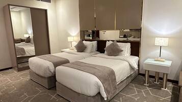 A hotel room with two beds, a large mirror, a bedside table with a lamp, and a patterned carpet.