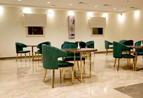 A conference room with green upholstered chairs and a round table, featuring a painting on the wall and recessed ceiling lights.