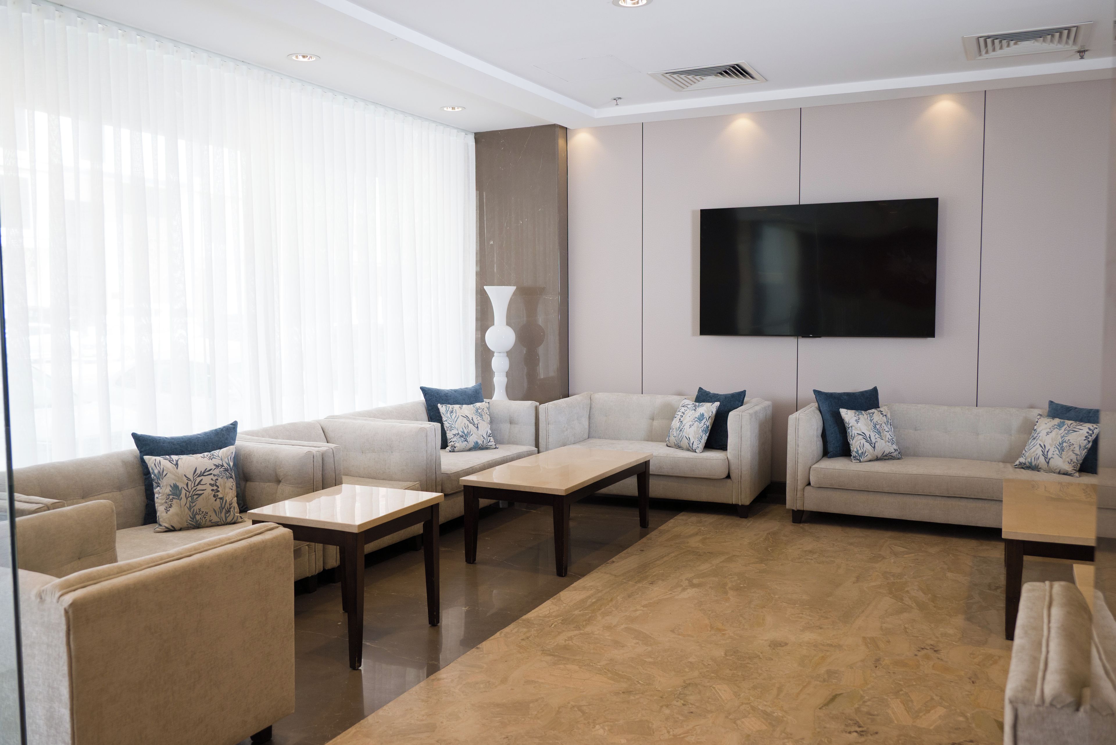 A modern living room with a flat-screen TV mounted on the wall, two sofas with patterned cushions, a coffee table, and a floor lamp.
