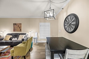 Una sala de estar con un sofá negro, un sillón amarillo, una mesa de comedor y un reloj de pared grande.
