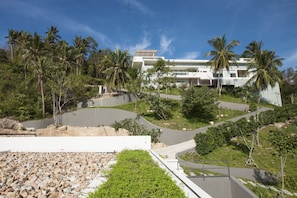 Um hotel moderno com uma entrada sinuosa, palmeiras e um céu azul límpido.