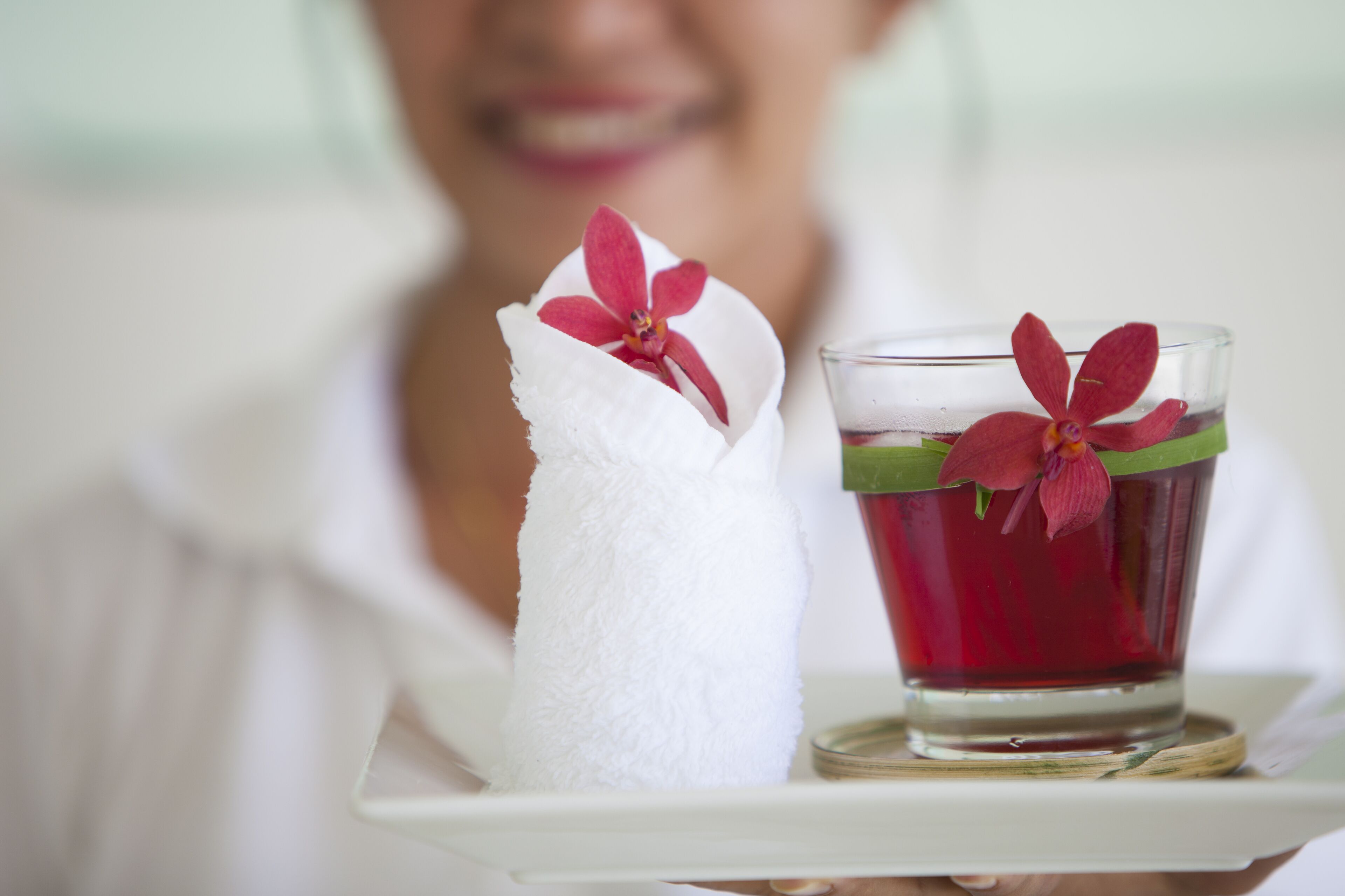 A white towel with a red flower and a glass of red drink with a green leaf on a tray.