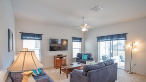 A living room with a sofa, a coffee table, a lamp, a TV, and a ceiling fan. - South-Facing Private Pool • 2 Ensuites • 15 Minutes to Disney (Davenport)