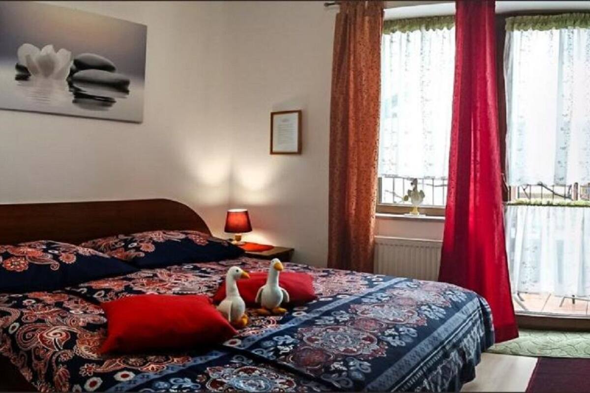 Een slaapkamer met een bed, kussens, een ingelijst beeld, een lamp en een raam met gordijnen.
