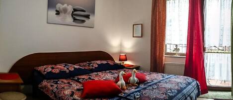 Un dormitorio con cama, almohadas, un cuadro enmarcado, una lámpara y una ventana con cortinas.