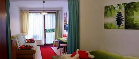 Habitación de hotel con cama, sofá, escritorio y silla. Se ve una ventana con cortinas, un cuadro en la pared y una alfombra roja en el suelo.