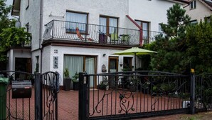 A two-story building with a balcony, a green umbrella, and a brick pathway leading to a gated entrance. - Willa Christo Dom z Dusza (Kolobrzeg)