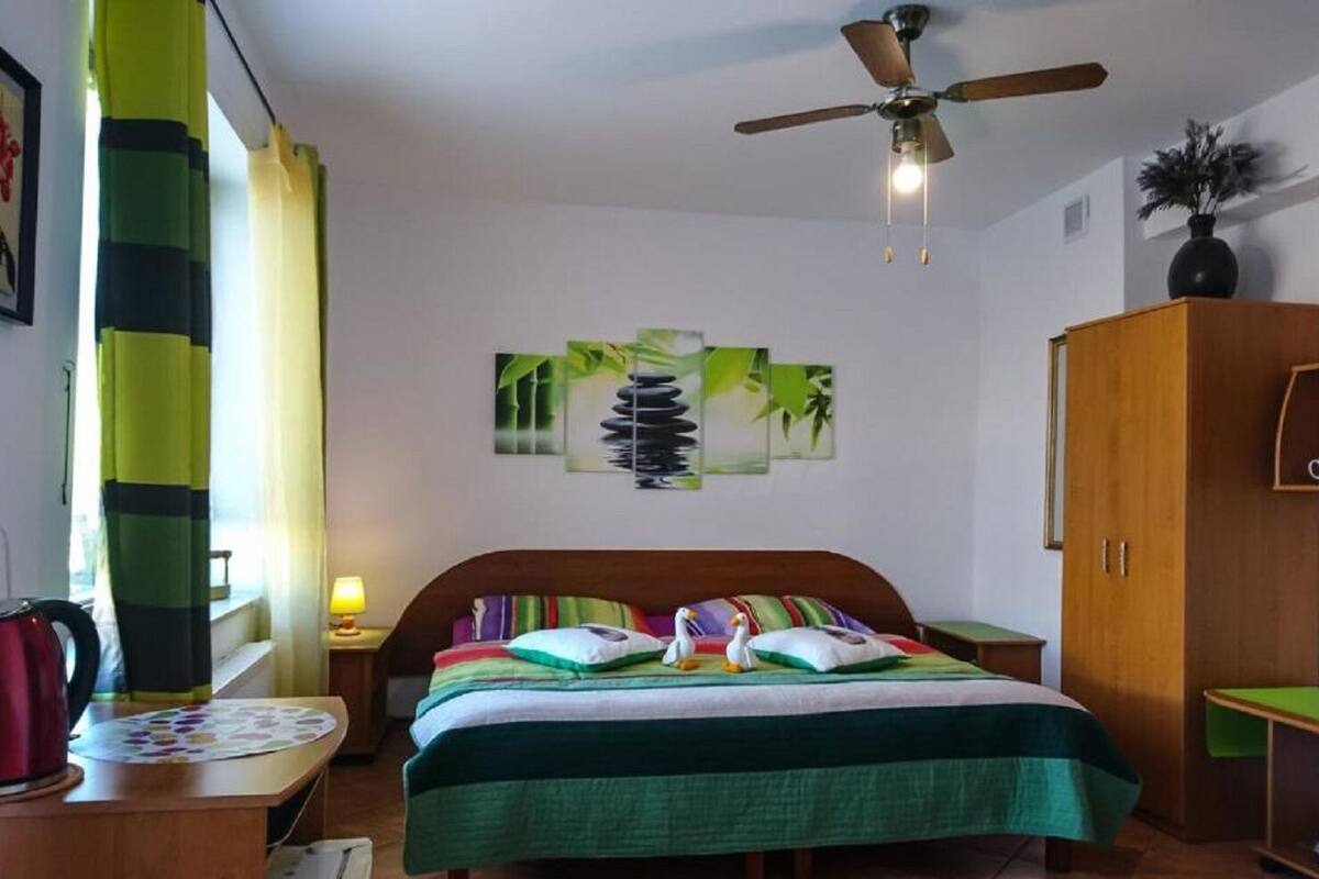 Een slaapkamer met een bed, een plafondventilator, een nachtkastje, een lamp, een kledingkast en een raam met gordijnen.