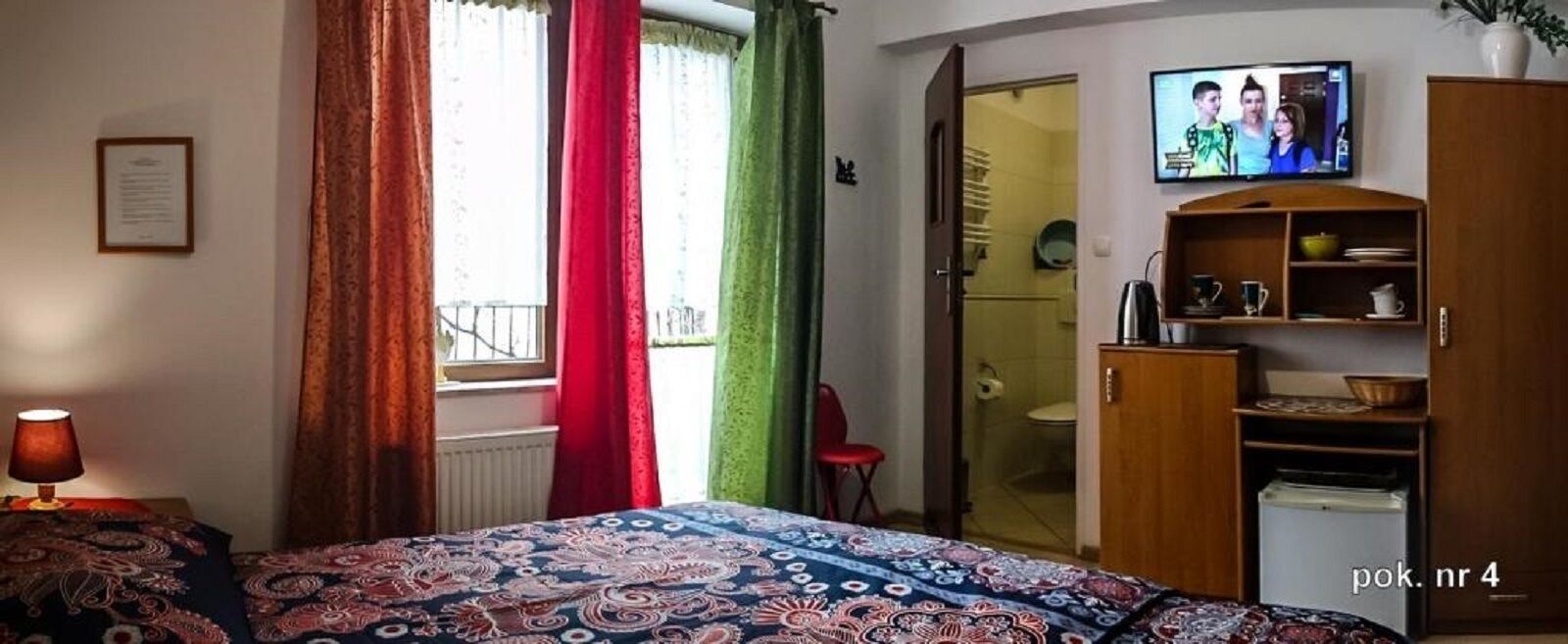 Un dormitorio con cama, televisor, armario y una silla roja.