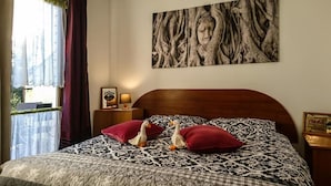 A bedroom with a patterned bedspread, two pillows, a nightstand with a lamp and a framed picture, and a large wall painting. - Willa Christo Dom z Dusza (Kolobrzeg)