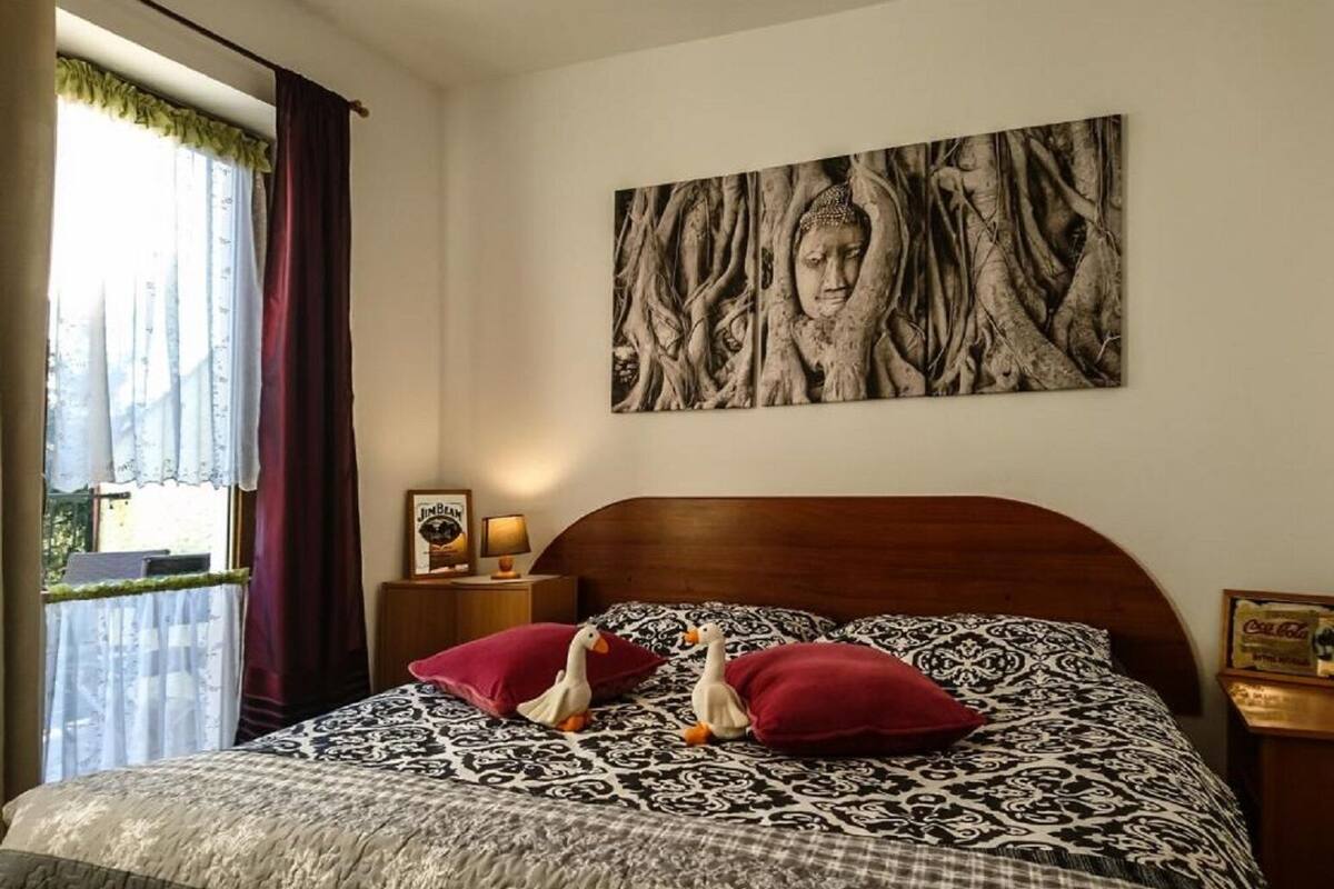 Een slaapkamer met een bed met een geborduurd sprei, twee kussens, een nachtkastje met een lamp en een ingelijst beeld, en een groot muurschilderij.