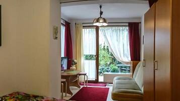 A room with a bed, a desk, a chair, a sofa, a window with curtains, and a painting on the wall.