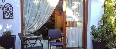 Un patio con una mesa, dos sillas, un adorno de pared y plantas en macetas.