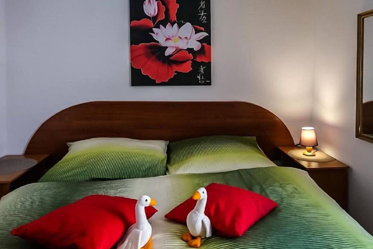 Een net opgemaakt bed met groene en rode kussens, een houten hoofdbord en een wandlamp.