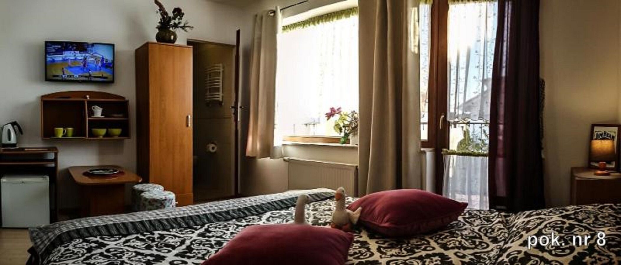 Quarto de hotel com duas camas, televisão, guarda-roupa e janela com cortinas.
