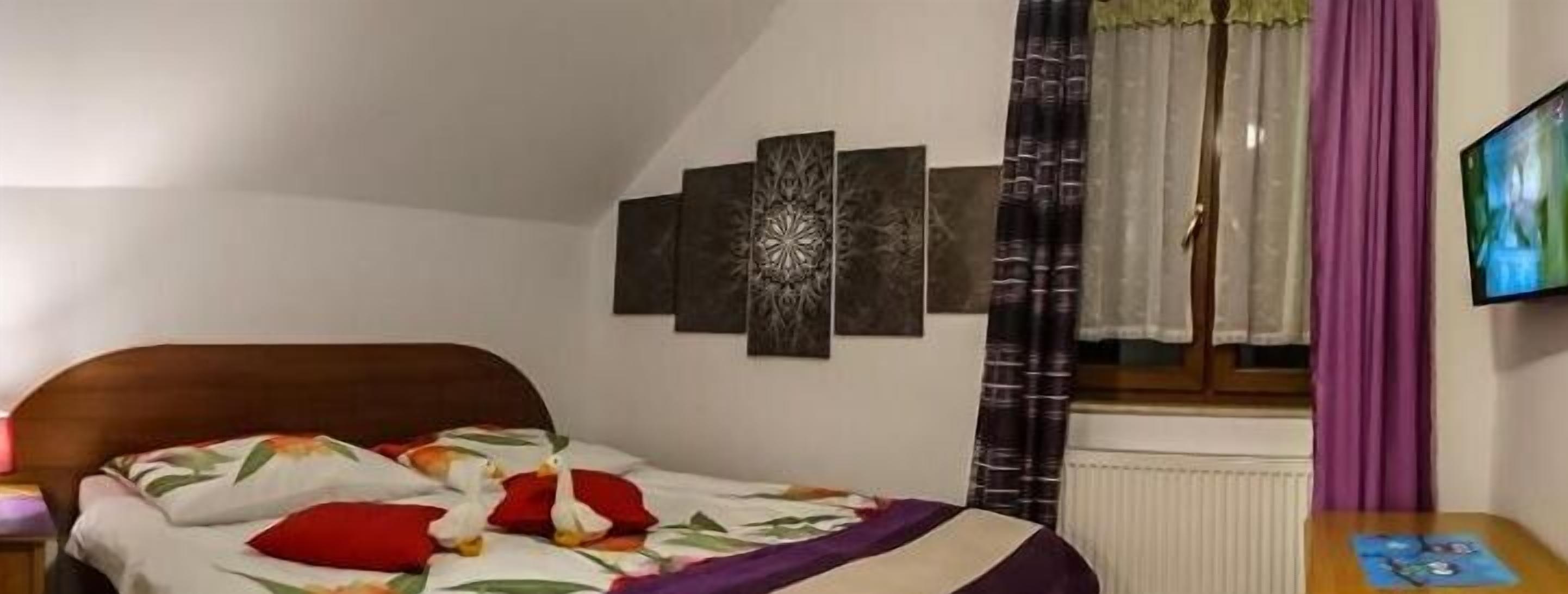 Una camera da letto con un letto, un comodino, una TV a parete e una finestra con tende.