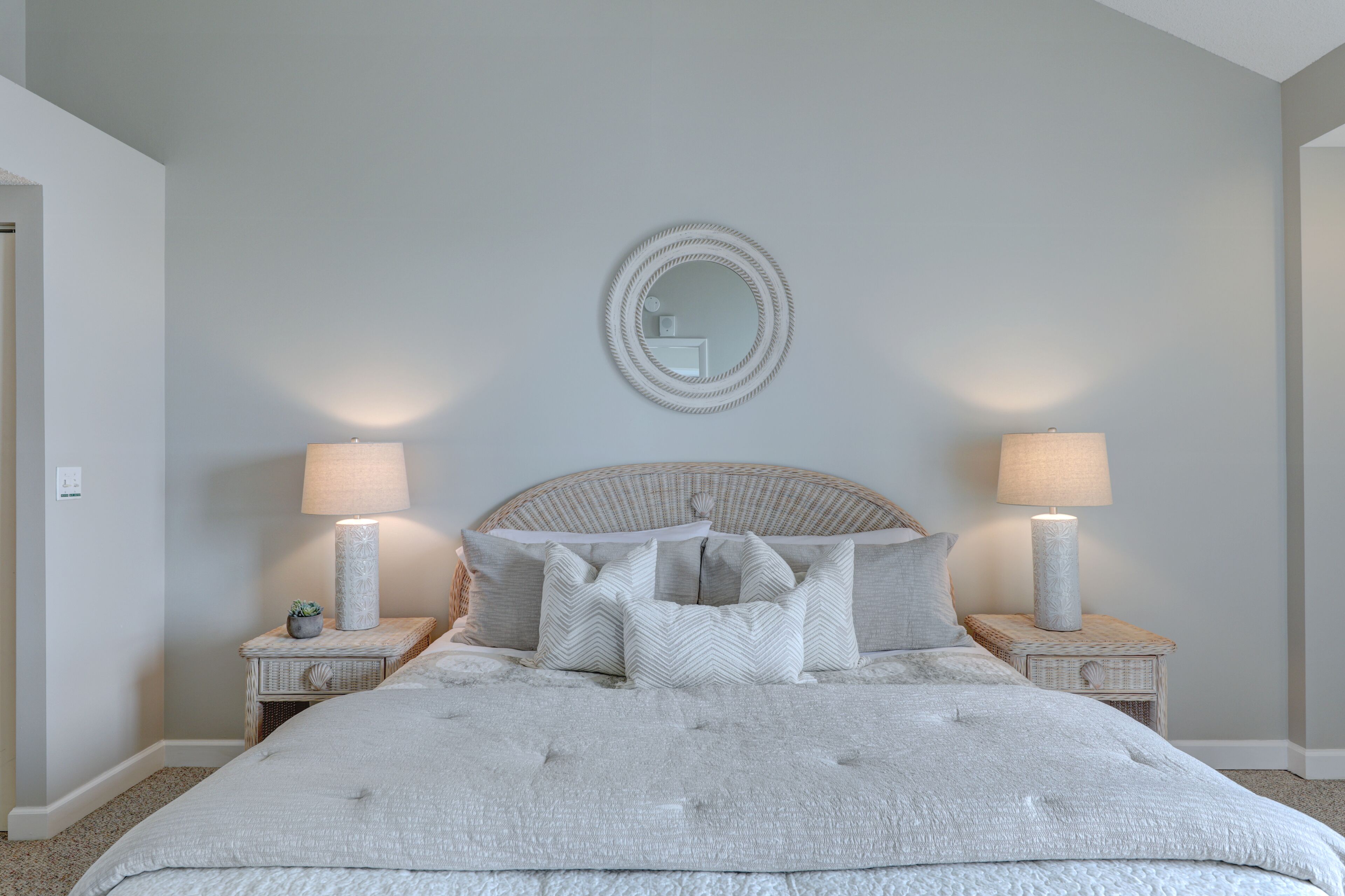 Une chambre à coucher avec un grand lit, deux tables de chevet, un miroir rond et deux lampes fixées au mur.