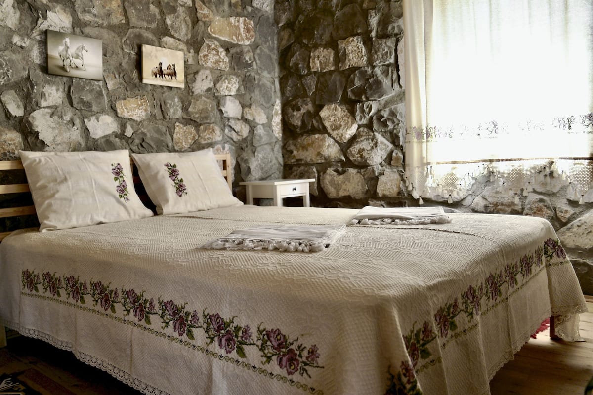 A bedroom with a stone wall, a bed with floral bedding, and two bedside tables.