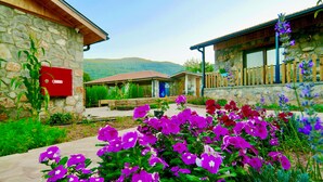 A stone building with a red electrical box, a wooden deck, and a garden with purple flowers. - Dedehan Retreat Otel (Fethiye)
