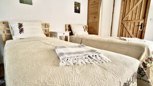 A room with two beds, each with a white bedspread and a decorative pillow. There is a wooden door and a small white table in the room. - Dedehan Retreat Otel (Fethiye)