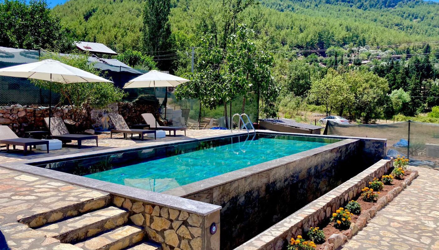 Piscina com degraus de pedra e espreguiçadeiras e guarda-sóis ao redor.