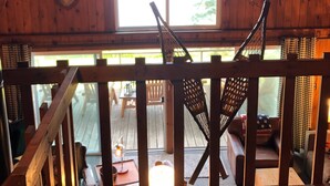 A wooden cabin with a balcony, a large window, and a hanging deer head decoration. - Cozy lakefront chalet with cedar hot tub + stunning lake views (Remer)