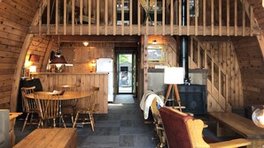 A rustic wooden interior with a dining area, a fireplace, and a loft space. - Cozy lakefront chalet with cedar hot tub + stunning lake views (Remer)