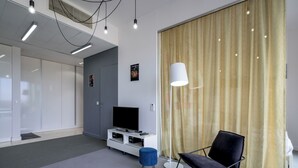Een moderne woonkamer met een flatscreen televisie, een blauwe poef, een zwarte stoel en een vloerlamp.