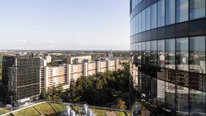 Een hoog gebouw met een glazen gevel met uitzicht op een stadsbeeld met diverse gebouwen en een kerktoren in de verte.