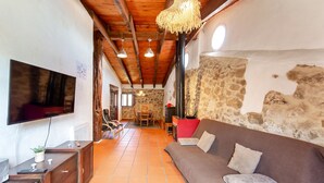 A cozy living area with a sofa, TV, wooden ceiling beams, stone wall, and a fireplace.