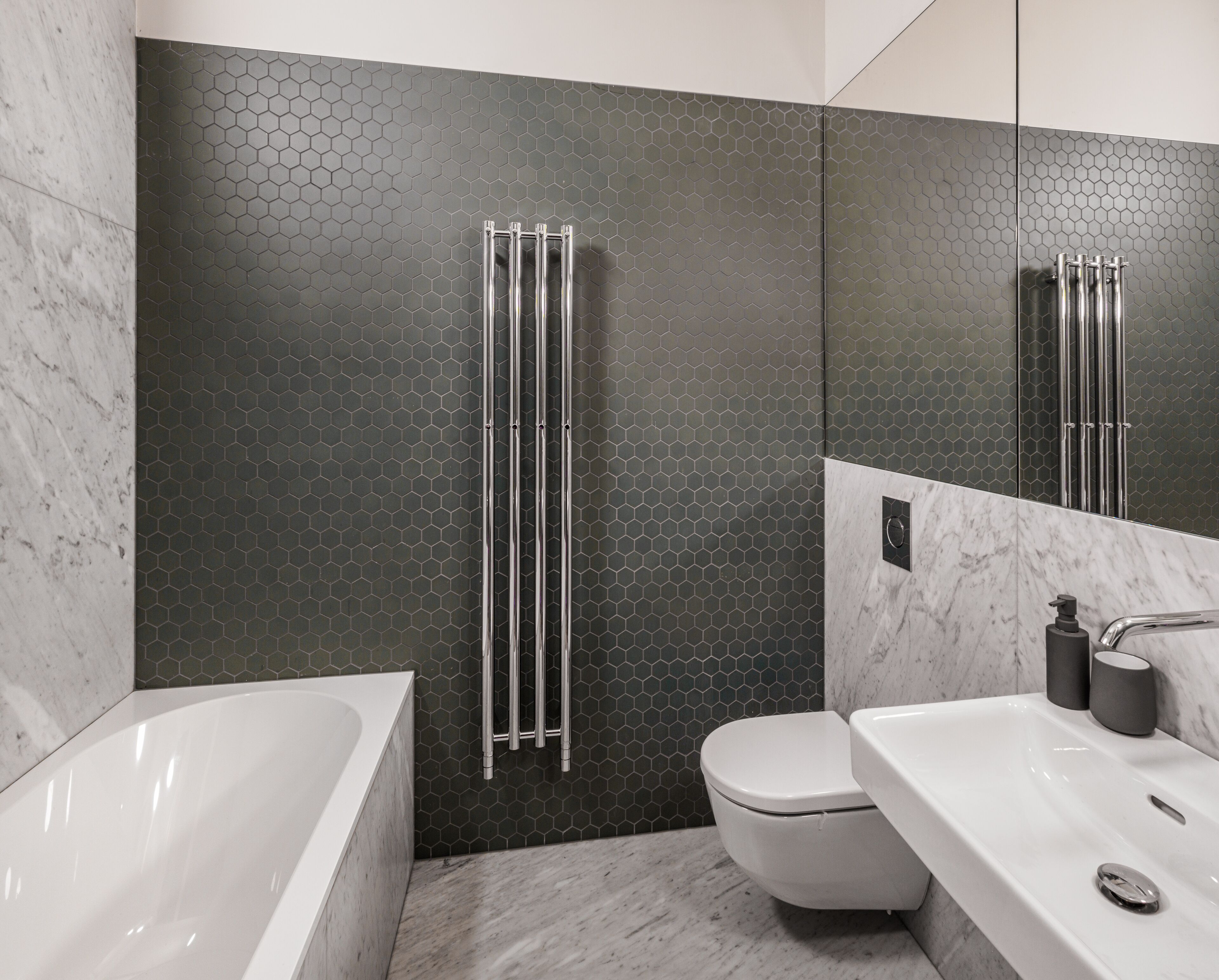 Un baño moderno con un salpicadero de azulejos hexagonales, un inodoro blanco, una bañera y un lavabo con un espejo encima.