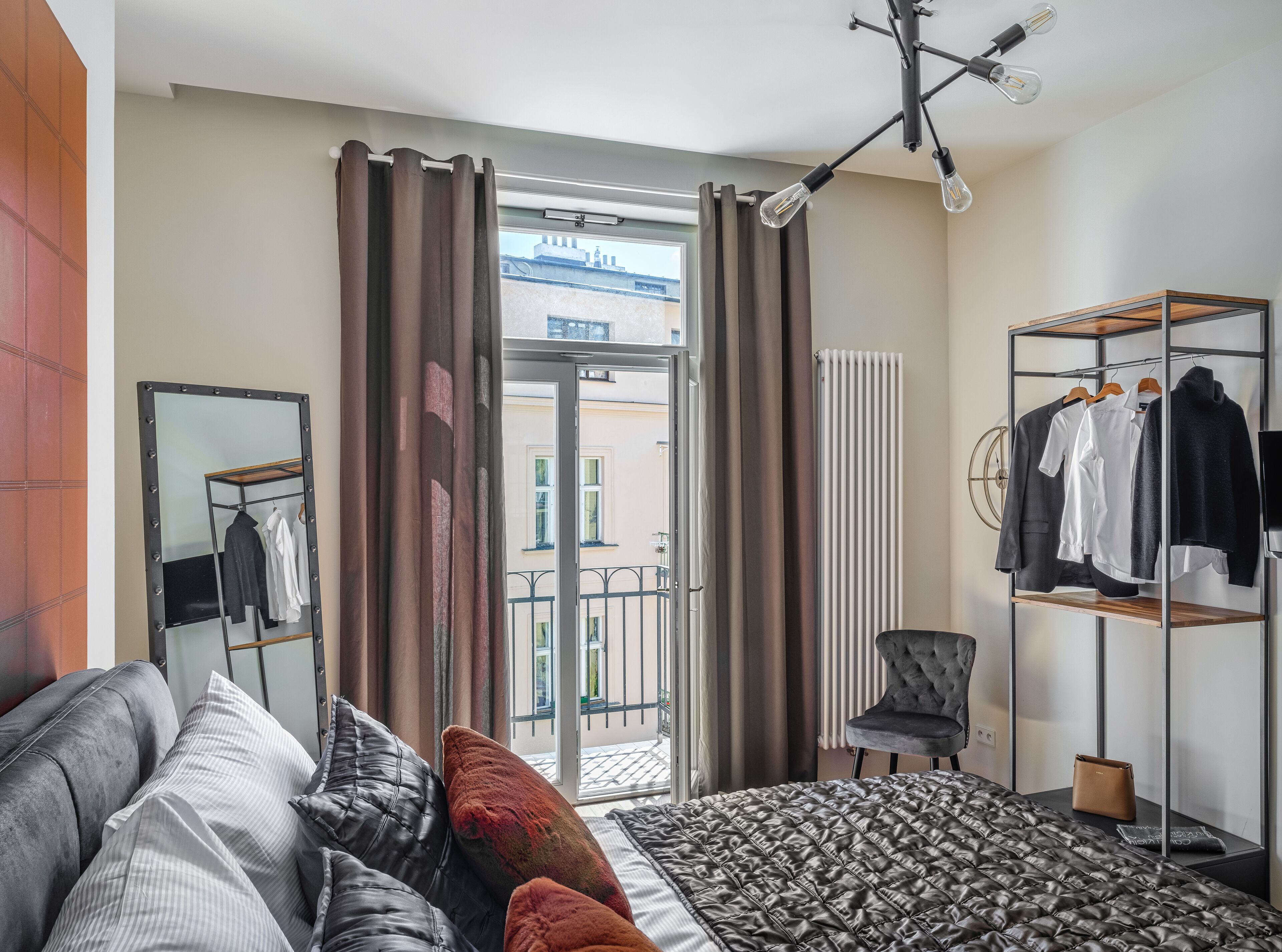 A modern bedroom with a bed, a wardrobe, a mirror, and a view of the outside.