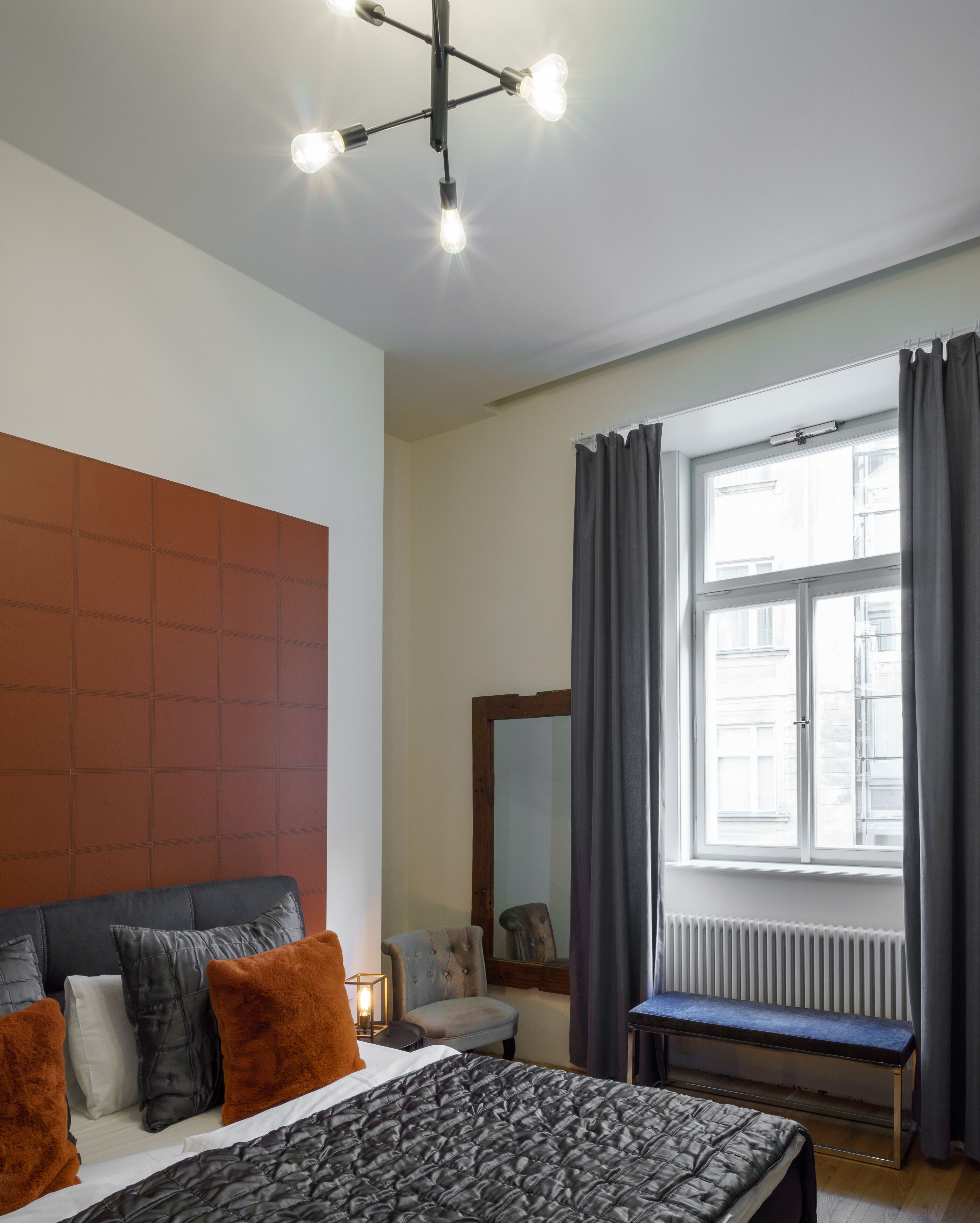 Un dormitorio con una cama, un banco, una silla, un espejo y una ventana con cortinas.