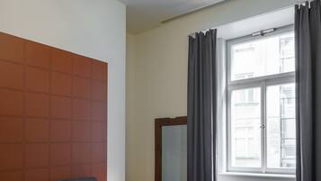 Un dormitorio con una cama, un banco, una silla, un espejo y una ventana con cortinas.