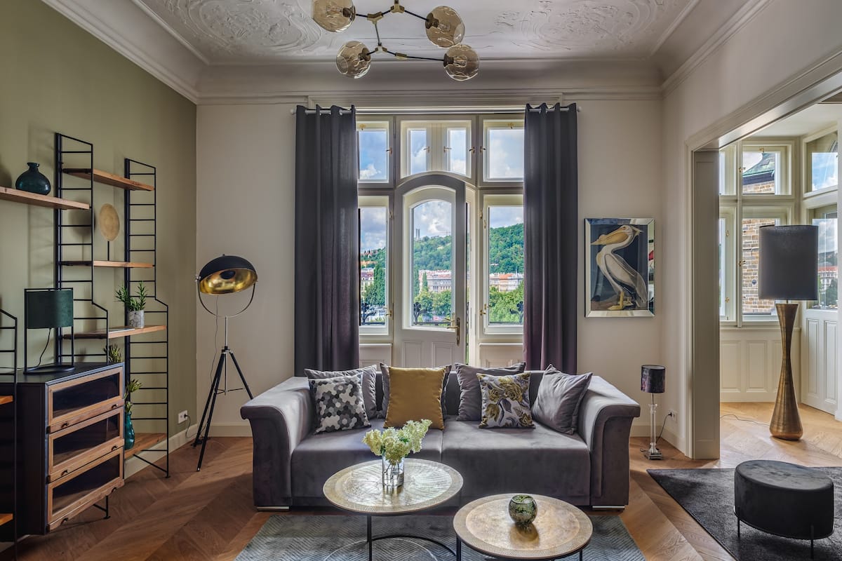 A living room with a sofa, two side tables, a floor lamp, a bookshelf, and a large window with curtains.