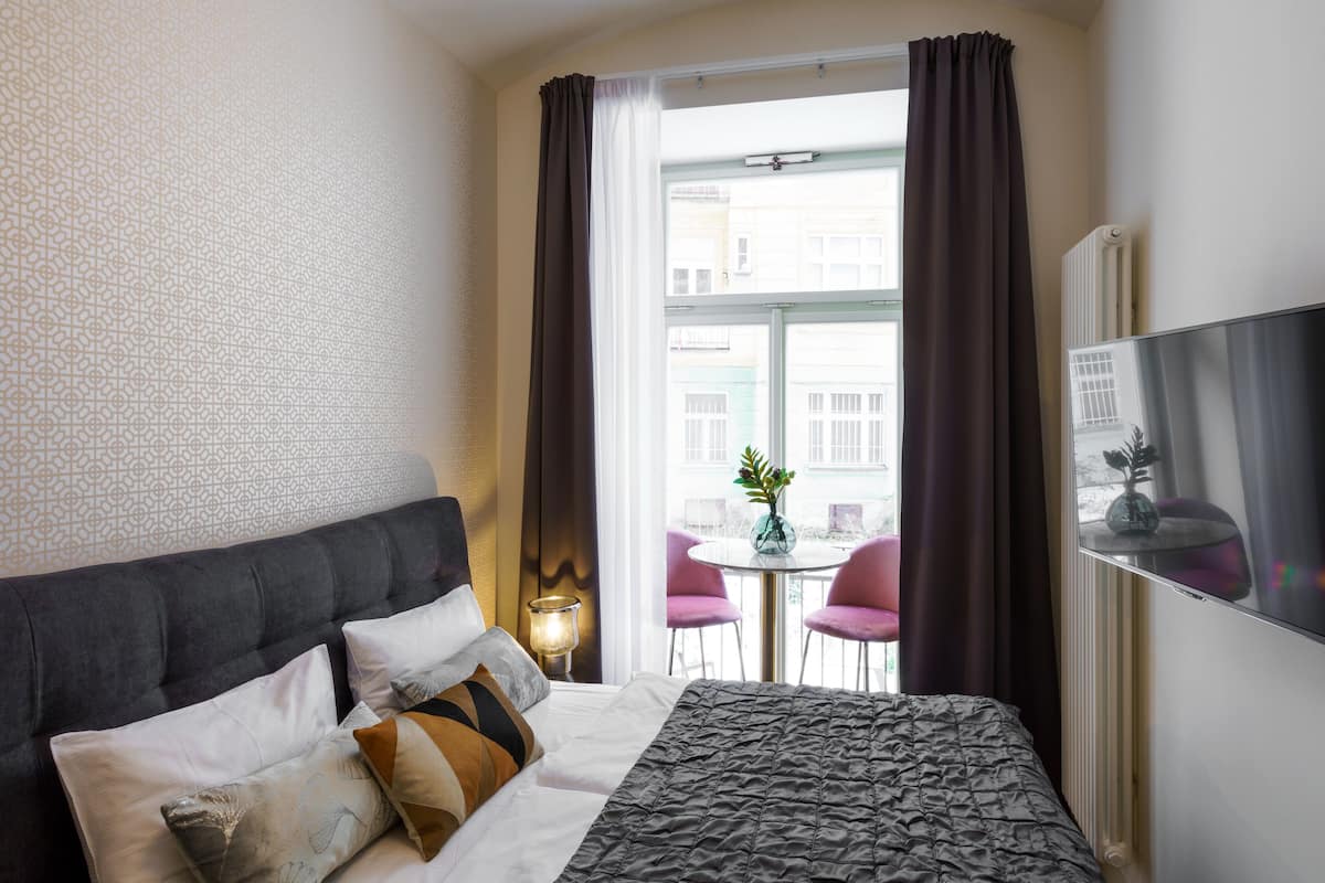 A hotel room with a bed, a TV, a window with curtains, and a view of the outside.