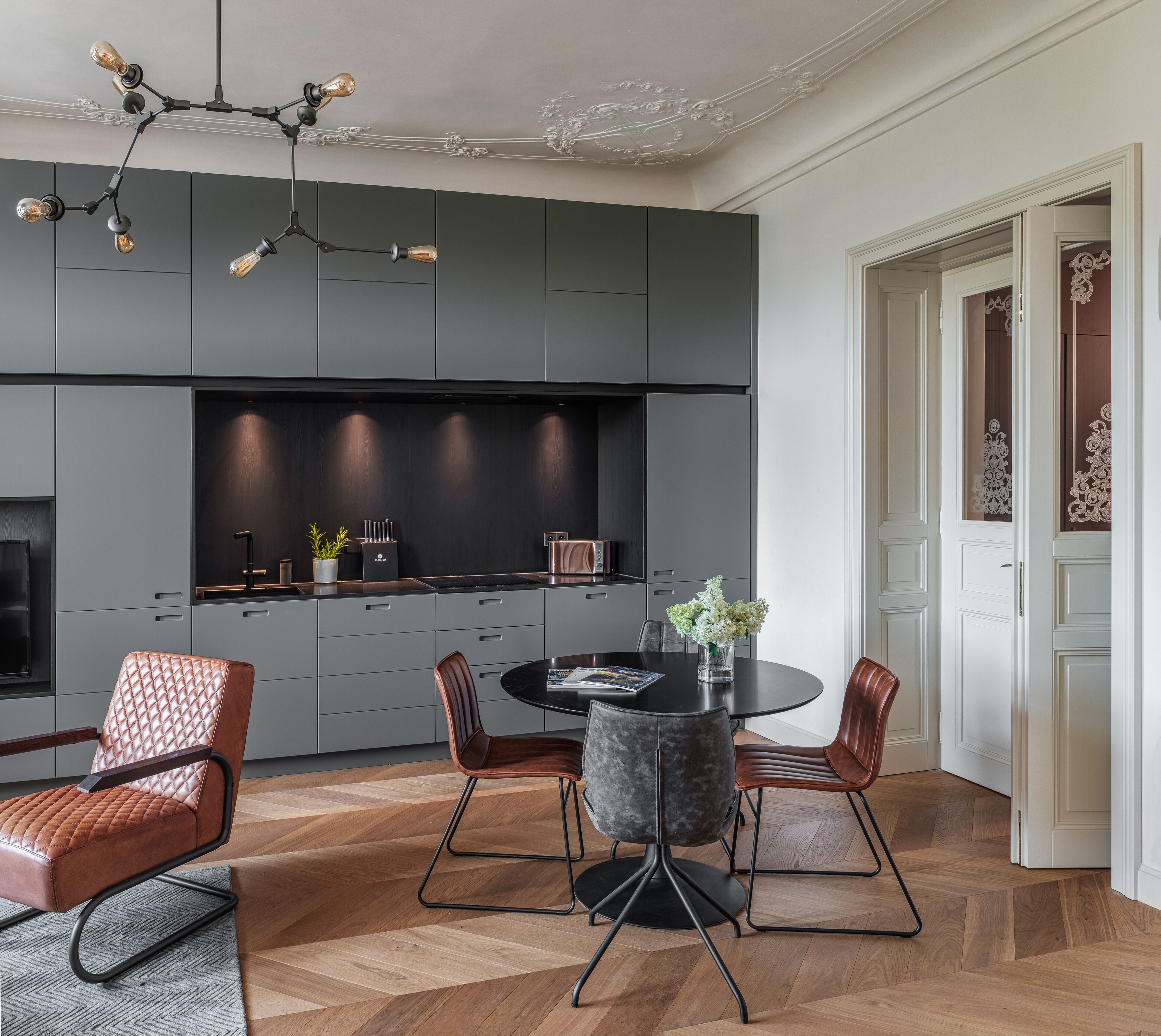 A modern kitchen with dark cabinetry, a round dining table, and a chandelier.