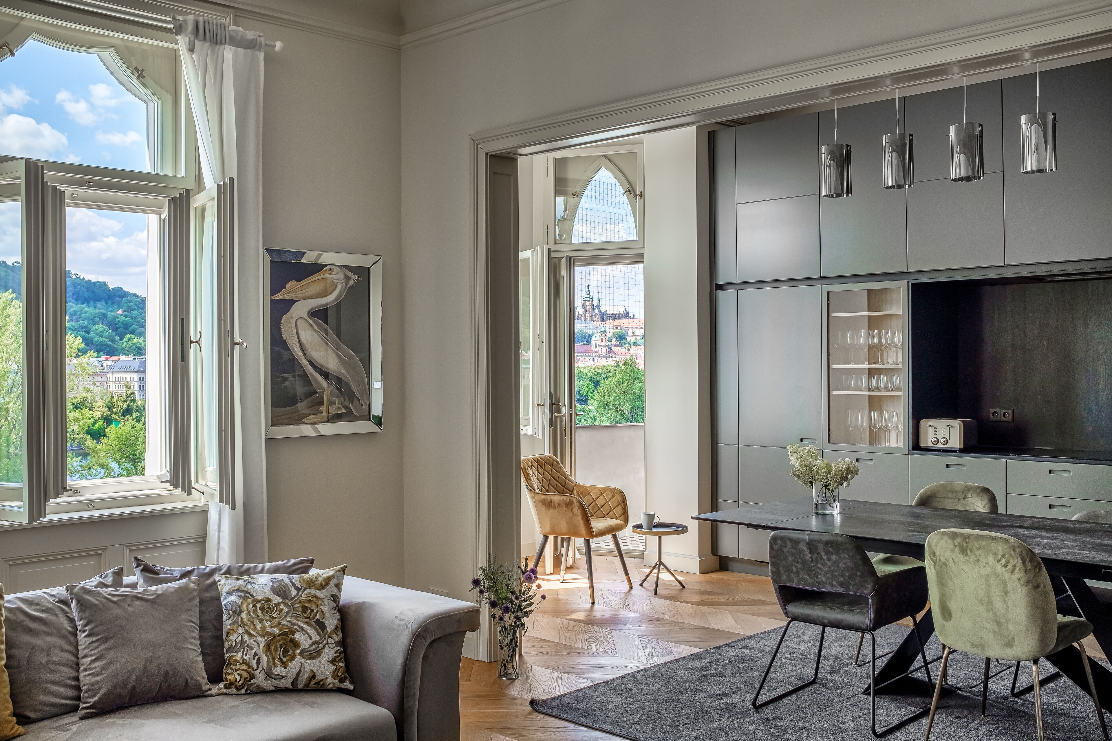 A modern living room with a sofa, a dining table, and chairs. There is a view of a cityscape through large windows.