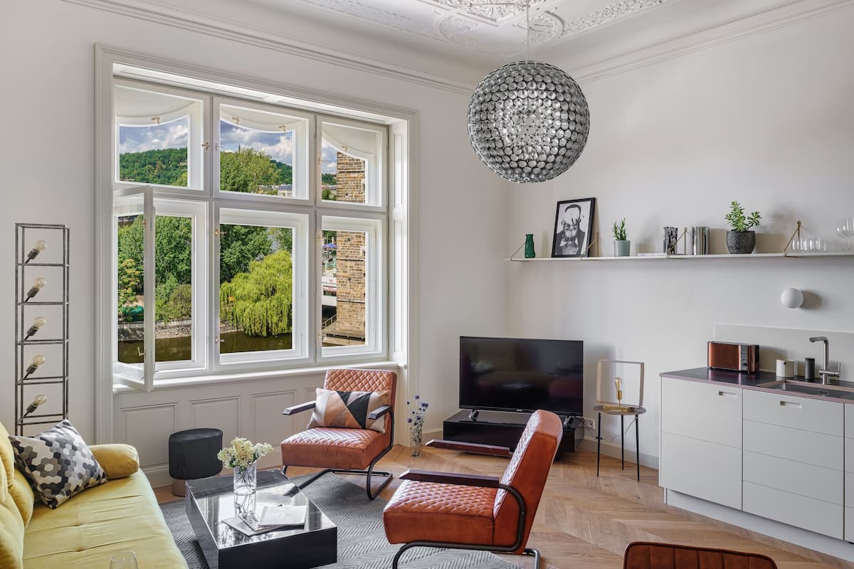 A modern living room with a large window, a flat-screen TV, a sofa, a coffee table, and a kitchen area with a toaster.