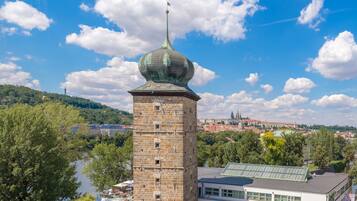 A historic tower with a green dome, surrounded by lush greenery and a river.