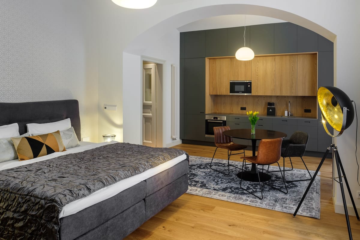 A modern bedroom with a large bed, a dining area with a table and chairs, and a kitchen with wooden cabinets and a microwave.