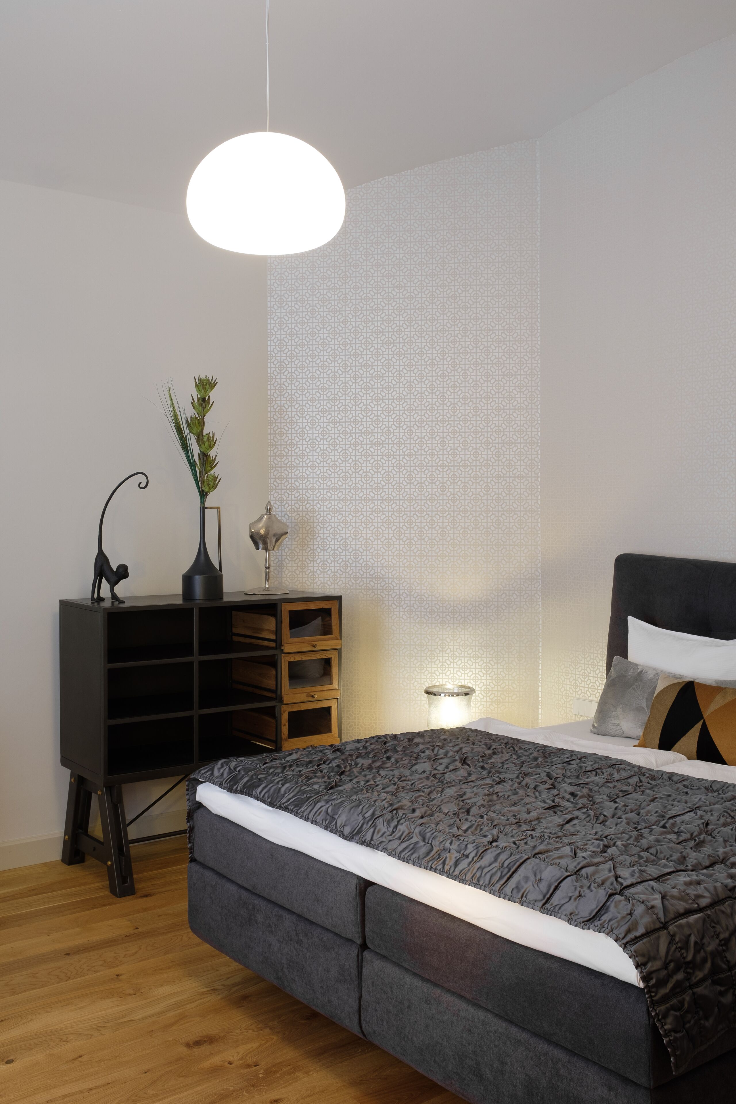 Een slaapkamer met een groot bed, een nachtkastje, een lamp, een dressoir en een hangende lamp.