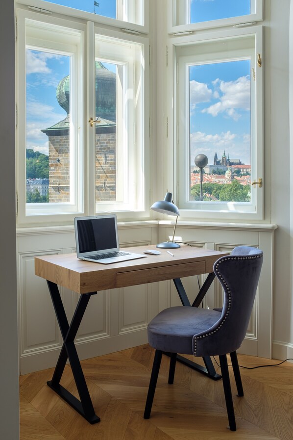 Un escritorio con una computadora portátil, una lámpara y una silla en una habitación con ventanas amplias que dan a una vista panorámica de la ciudad.